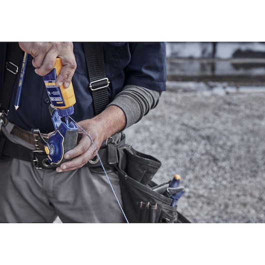 Close-up photo of worker using IRWIN chalk reel IWHT48443, filling with chalk powder, tool belt visible.