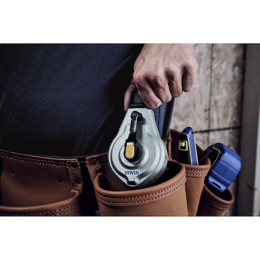 IRWIN IWHT48445 chalk line tool held in hand, placed in brown leather tool belt pouch.